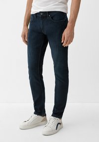 Donkerblauwe denim jeans met een slim fit, voorzien van vijf zakken, een knoopsluiting en subtiele stikdetails. Gecombineerd met witte sneakers.
