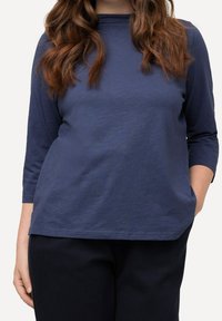 Navy long-sleeve top with a round neckline, featuring a relaxed fit and soft, textured fabric, paired with dark pants.