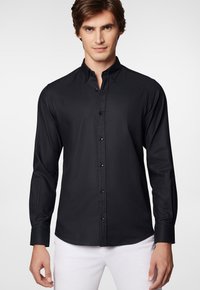 Czarna, długa koszula z guzikami o dopasowanym kroju. Posiada tradycyjny kołnierzyk, czarne guziki i gładką teksturę materiału. Prosty i elegancki design.