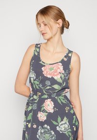 Vestido floral com um fundo em azul marinho escuro, apresentando grandes flores pink e verdes, decote arredondado e um ajuste relaxado com bolsos laterais.