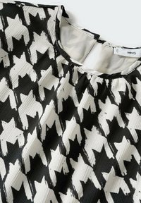 Blouse noir et blanc à motifs avec formes géométriques abstraites, encolure ronde, détail de tissu froncé et étiquette intérieure visible.