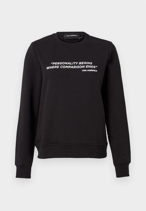 Svart sweatshirt med rund hals, lange ermer. Har hvit tekst: "PERSONLIGHETEN BEGYNNER DER SAMMENLIGNING SLUTTER" på forsiden. Glatt tekstur.