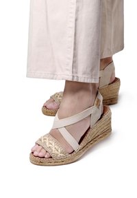 Beige espadrille platvormsandlid, millel on kootud kangast pealmine osa, elastsed rist-öösid ja juutiga kaetud tald; jalg osaliselt nähtav.