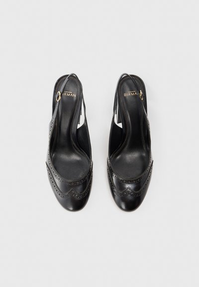 Svarta läderslingback-skor med scallop-design och perforeringar, öppen tå, och en dekorativ guldfärgad detaljer på hälen.
