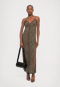 Abito maxi animalier in beige e nero, con spalline sottili, scollatura a V profonda, spacchi laterali e una superficie liscia. Abbinato a una borsa nera.