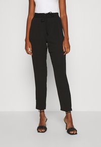 Zwarte, lichtgewicht tapered broeken met een trekkoord in de taille, met een gladde textuur en subtiele draping, gecombineerd met zwarte sandaalhakken.
