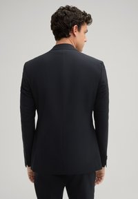 Zwarte blazer, op maat gemaakt ontwerp, gestructureerde schouders, gladde textuur, enkele split aan de achterkant en knoopmanchetten.