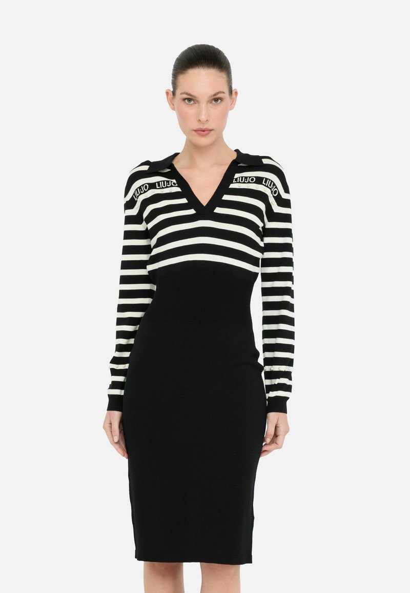 Robe en tricot à rayures noires et blanches avec un décolleté en V, des manches longues et des détails côtelés à la taille et aux poignets. Accent sur le logo aux épaules.