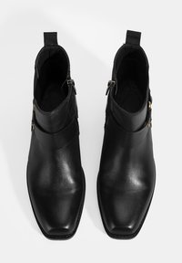Bottes chelsea en cuir noir avec une texture lisse, un design à bout carré, des fermetures éclair latérales et des accents en métal doré.