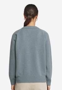 Helles blaues Strickpullover mit geripptem Saum und Bündchen, ausgestattet mit einem runden Ausschnitt. Der Stoff wirkt weich und strukturiert.