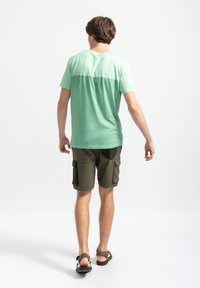 Lichtgroen T-shirt met korte mouwen met een gradient ontwerp, gecombineerd met olijfgroene cargoshorts met meerdere zakken. Zwarte sandalen.