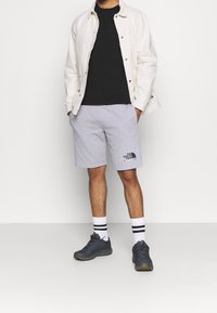 Gray shorts with logo, black t-shirt, and white buttoned jacket. Black shoes with green accents, white socks with black stripes.