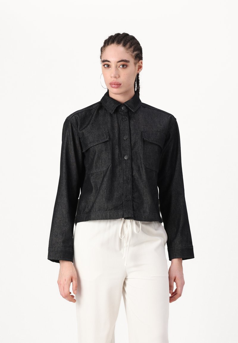 Chaqueta recortada de mezclilla negra con frente de botones, dos bolsillos en el pecho y mangas largas. Textura suave con detalles de costura mínimos.