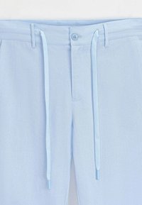 Pantalons bleu clair avec une taille à cordon, une fermeture à bouton et une texture lisse. Comprend des poches inclinées et une coupe ajustée.