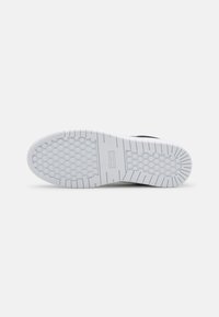 Semelle de chaussure en caoutchouc blanc avec des motifs circulaires antidérapants et des rainures droites, vue du dessous sur un fond clair uni.