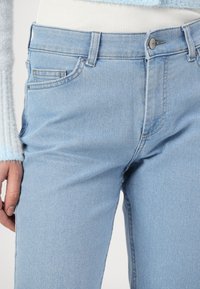 Μπλε τζιν παντελόνι σε ανοιχτό μπλε απόχρωση, με μέτρια κοιλιά, που διαθέτει κλείσιμο με κουμπί, μπροστινές τσέπες και λεία υφή.