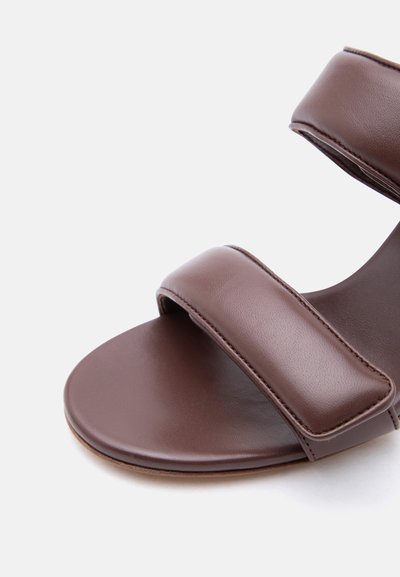 Καφέ δερμάτινο σανδάλι με δύο φαρδιές λουρίδες πάνω από το πόδι και τον αστράγαλο, με ομαλή υφή και εμφανή ραφές.