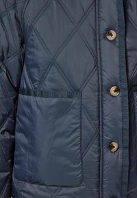 Tamsiai mėlynas siuvinėtas švarkas su deimanto raštu, žalvariniais mygtukais ir viena kišene su kontrastinga apdaila. Lygus paviršius.