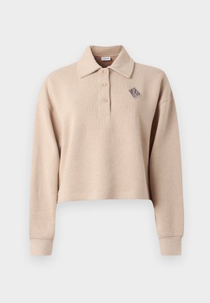 Beige cropped polotrøye med lange ermer, ribbet tekstur, tre knapper og en geometrisk logo i mørk blå på venstre brystområde.
