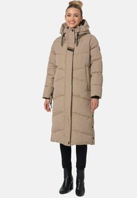 Long beige puffer coat with a hood, diagonal quilted pattern, two side pockets, and black drawstrings. Worn over black pants and boots.