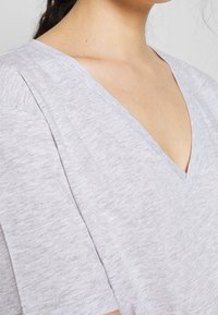 Camiseta de color gris claro con escote en V, fabricada en una suave tela texturizada. Cuenta con mangas cortas y un corte holgado, con detalles de costura sutiles.