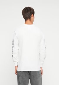 Wit katoen t-shirt met lange mouwen en een zwart decoratief patroon op de mouwen. Heeft een klassieke ronde hals en een ontspannen pasvorm.