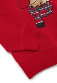 Felpa rossa con polsini a costine, caratterizzata da un'illustrazione di una renna che indossa una sciarpa a quadri. Materiale in cotone morbido e testurizzato.