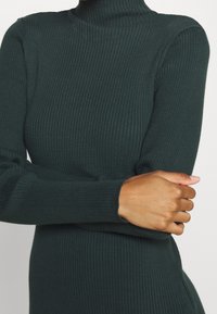 Vihreä ribattu neulepusero, jossa on pitkät hihat ja tyköistuva siluetti. Sujuva pinta, jossa on hieno venyvyys.