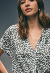 Leopardenmuster-Bluse aus leichtem Stoff mit V-Ausschnitt und kurzen Ärmeln. Grau- und schwarzes Muster auf hellem Hintergrund.