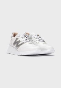Zapatillas blancas de material de cuero texturizado y acabados metálicos plateados. Presentan una suela blanca gruesa y cordones grises. Logo distintivo en el lateral.