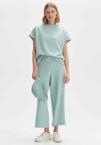 Un top en tricot texturé bleu clair associé à un pantalon large assorti et un chapeau, complété par des baskets blanches.