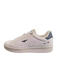 Sneaker bianco con superficie textured, caratterizzato da branding in rilievo, sottili accenti neri e verdi, e design della punta arrotondato.