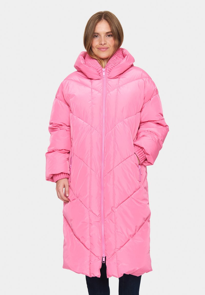 Hosszú rózsaszín puffasztott kabát kapucnival, steppelt textúrával és ferde varrással. Cipzáras záródás és oldalsó zsebek találhatók rajta.