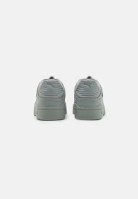 Un par de zapatillas Puma de color gris claro vista desde atrás, destacando el talón texturizado y el logo de Puma en cada zapato sobre un fondo blanco liso.