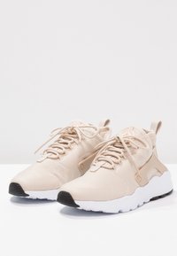 Beiga sportskor med en texturerad mesh-övre, snörning och en vit mellansula. Har en svart gummisula för bättre grepp.