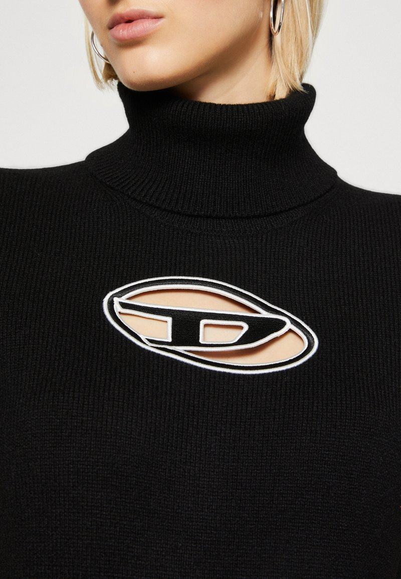 Schwarzer gerippter Rollkragenpullover mit einem ausgeschnittenen Logo in kontrastierendem Weiß und Beige. Die eng anliegende Passform betont die Textur und Details.