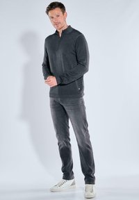 Grauer Reißverschluss-Pullover mit langen Ärmeln und subtiler Textur, kombiniert mit grauen Jeans und weißen Sneakers, vor einem schlichten Hintergrund.