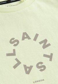 Svetlozelené bavlnené tričko s okrúhlym grafickým prvkom, na ktorom je napísané "ALLSAINTS" hnedou farbou. Hladký okraj výstrihu s detailom štítku na zadnej strane.