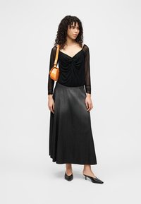 Μαύρο μπλουζάκι με μακριά μανίκια, γκρι τζιν μάξι φούστα, μαύρα τακούνια και πορτοκαλί τσάντα ώμου. Λεπτό ύφασμα με λεπτομέρεια σφιγμένης μέσης.