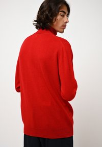 Roter, weicher Strickpullover mit hohem Kragen und lockerer Passform. Mit strukturiertem Finish, gerippten Bündchen und Saum. Einfaches Design ohne sichtbare Muster oder Akzente.