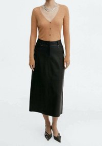 Hnědý žebrovaný cardigan s knoflíky, zkombinovaný s černou koženou midi sukni. Černé lodičky s špičatou špičkou dokončují tento vzhled. Součástí je stříbrný víceřadý náhrdelník.