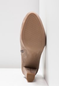 Chaussure à talon en daim marron montrant une semelle texturée antidérapante, un bout pointu et un talon bloc sur fond blanc.