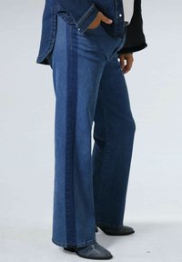 Uitlopende denim jeans in een donkere indigo was, met een contrasterende zijsstrip, zakdetails en een lichte textuur. Gecombineerd met donkere laarzen.