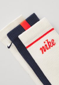 Trois paires de chaussettes : crème et marine avec une texture côtelée, des accents rouges, et "nike" en broderie rouge sur la paire crème.