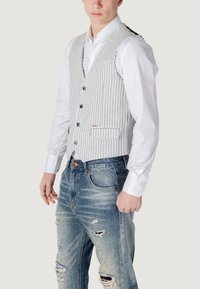 Gilet grigio a righe con cinque bottoni, una tasca e una vestibilità aderente. Abbinato a jeans blu strappati, con strappi e un lavaggio sbiadito.