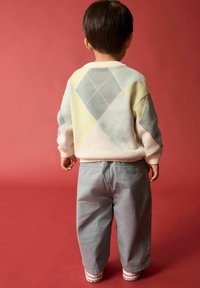 Pull en couleur pastel, texturé, avec un motif en losanges bleu clair, jaune et rose ; associé à un pantalon ample gris clair et des baskets.