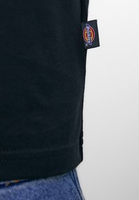 Black cotton t-shirt featuring a stitched hem and a small Dickies logo tag on the side. The fabric appears smooth with a relaxed fit.