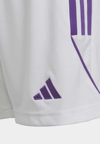 Witte sportshorts met paarse accenten en drie verticale strepen. De stof lijkt glad, met een klein geborduurd logo.