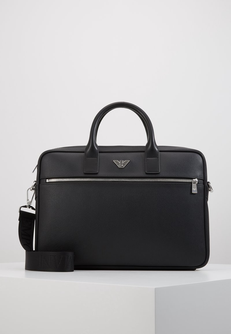 Mallette en cuir noir avec double poignée, poche avant zippée et bandoulière amovible, avec emblème de logo argenté.