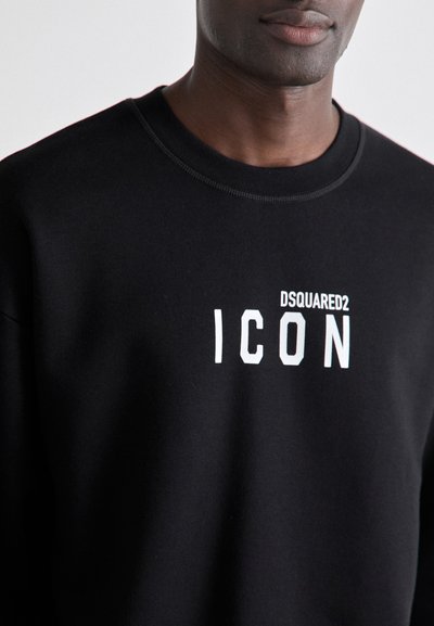 Must黑色 puuvillane sünnipäevajakk ümarate kaelustega. Esiküljel on julge valge tekst "DSQUARED2 ICON". Sujuv, pehme tekstuur.